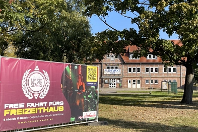 Freizeithaus durch Bäume fotografiert mit einem Protestbanner im Vordergrund