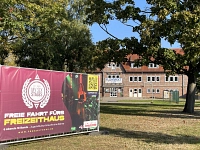 Freizeithaus durch Bäume fotografiert mit einem Protestbanner im Vordergrund