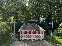 Vor einer Holzbrücke steht ein Absperrgitter