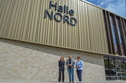 Drei Personen stehen vor einer riesigen Sporthalle mit der Aufschrift Halle Nord.&nbsp;&copy;&nbsp;Hansestadt Buxtehude